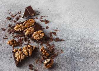 chocolate bar pieces with walnuts on grey background with chocolate crumbs. 