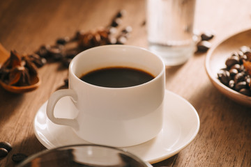 A cup of coffee with water, coffee beans and tea on wooden bakcground