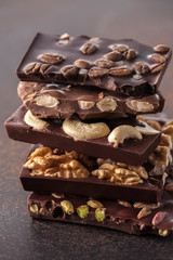 chocolate bar pieces with pistachios, cashew nuts, coffee beans, filbert and walnuts on brown background.