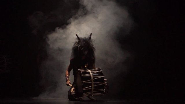 Four artists drummers Taiko in a wig with horns and make-up drum on stage against a dark background with smoke. Demons from Japanese mythology.