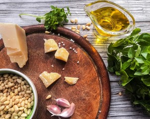 Ingredients for making pesto sauce: garlic cloves in the foreground, on a blurred background: green Basil, Parmesan cheese, olive oil, pine nuts on a wooden background. Selective focus