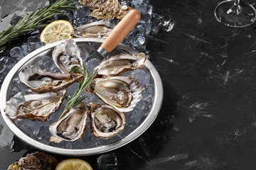 Fresh opened oysters, ice and lemon on a round metal plate, black stone textured background. Top view with copy space. Close-up shot.