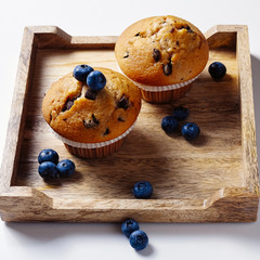 Muffins and bluebeeries on wooden tray over white background