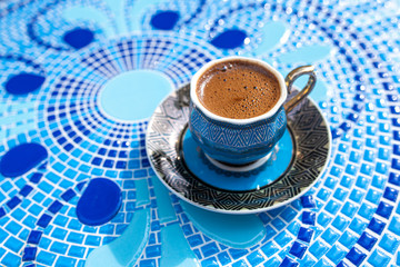 Cup of coffee on ornate blue mosaic background, with copy space