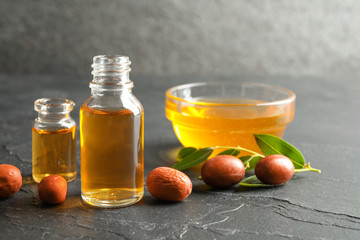 Jojoba oil and seeds on dark grey table