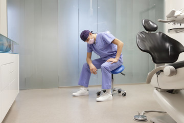 Tired dentist in his office sitting on stool, having break,waiting for patient in his office