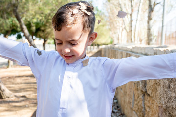Happy arabic boy enjoying playing with dried leaves outside in th park