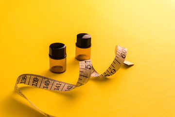 Empty bottle with a measuring tape, diet or healthy eating concept, Yellow background with soft...