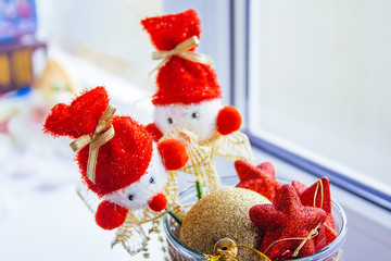 A vase stands at the window filled with red and yellow Christmas tree toys. Two snowmen on sticks are on top.