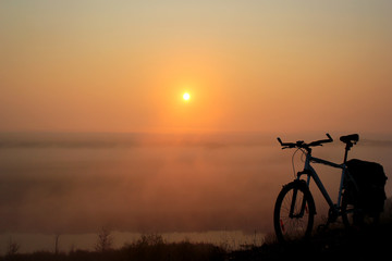 Fototapeta na wymiar Bike ride at sunrise. Bicycle, morning mist and orange sun.