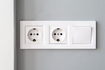 A closeup view of a group of white european electrical outlets and a switch located on a gray wall