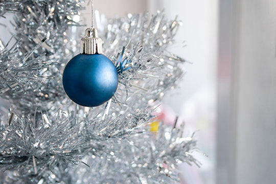 Closeup view of a blue matte ball hanging on a silver artificial Christmas tree