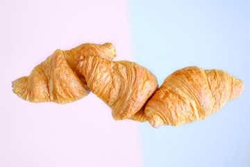 Three freshly baked croissants fly on pink and blue background. Place for text. Creative bakery concept.