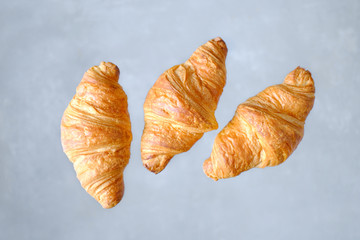 Three freshly baked croissants fly on grey background. Place for text. Creative bakery concept.