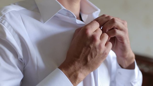Man buttons up his white shirt standing in the front of a bright window. Man buttoning his shirt. Close-up.