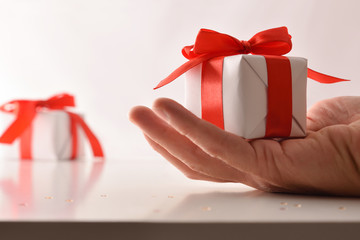 Hand with white gift and red bow on table front
