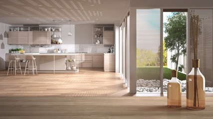Wooden table top or shelf with aromatic sticks bottles over blurred modern white kitchen with wooden details and island with stools, white architecture interior design