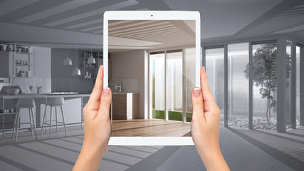 Hands holding tablet showing modern white and wooden kitchen, total blank project background, augmented reality concept, application to simulate furniture and interior design products
