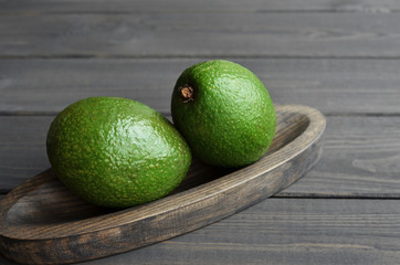 Two whole fresh avocado in wooden plate on dark wooden table background