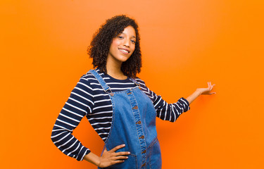 young pretty black woman feeling happy and cheerful, smiling and welcoming you, inviting you in...