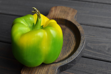 Organic green pepper in wooden plate on dark wooden table background, top view, copy space