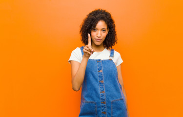 young pretty black woman smiling and looking friendly, showing number one or first with hand...