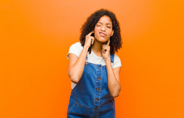 young pretty black woman looking angry, stressed and annoyed, covering both ears to a deafening...