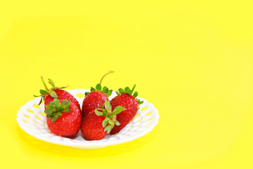 natural red strawberries with green leaves in a white decorative plate on a yellow background