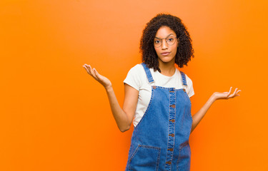 young pretty black woman feeling puzzled and confused, unsure about the correct answer or decision,...