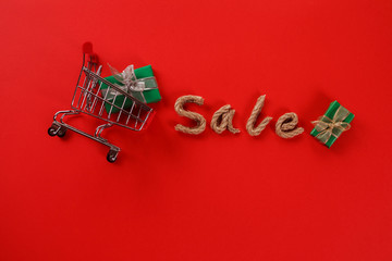 Christmas sale, rope letters om the red background, shopping cart with gift box in it