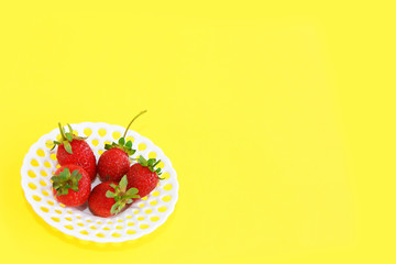 natural red strawberries with green leaves in a white decorative plate on a yellow background