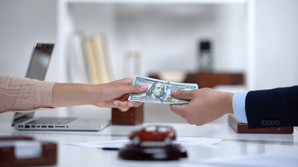 Female giving dollars to car dealer, down payment on brand new electric vehicle © motortion