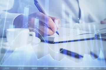 Double exposure of man's hands writing notes of stock market with forex chart.