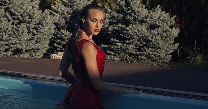 Woman in red dress is standing at the edge of the pool, walking out, 4k