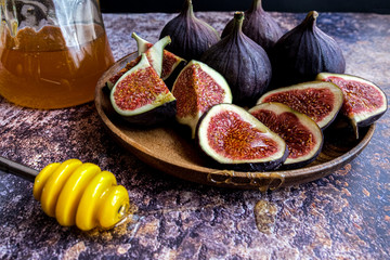 Whole figs and one fig sliced in half on top of a teak garden table. Focus is on the sliced fig. Fresh, all, half and quarter figs in a plate. Copy space.
