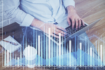 Double exposure of man's hands writing notes with laptop of stock market with forex graph...