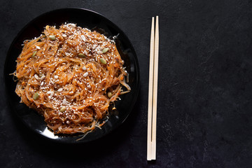 1 black plate brown Chinese cellophane rice noodles with shiitake mushrooms and peanut sauce, with sesame seeds on a dark background sticks ,