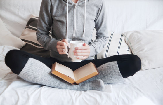 girl in home clothes on the couch reads a book and drinks a hot drink