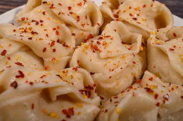 Boiled manti with beef on a plate with spices on a wooden table. Close up.