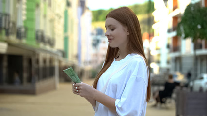 Excited teenage girl holding euro banknotes standing on street, first salary