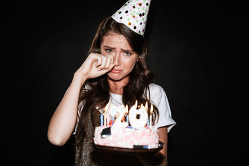 Image of beautiful upset woman holding cake with candles and crying
