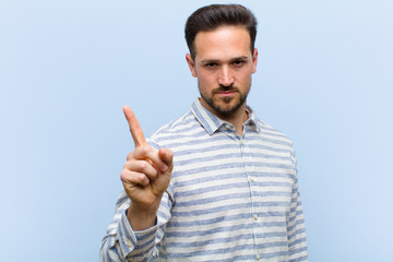 young handsome man feeling angry, annoyed, rebellious and aggressive, flipping the middle finger,...