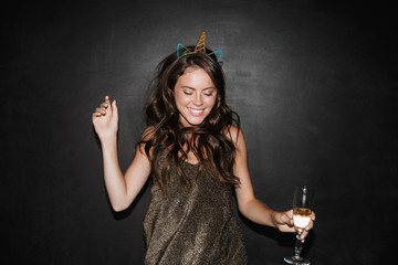Image of young smiling woman holding glass of champagne while dancing