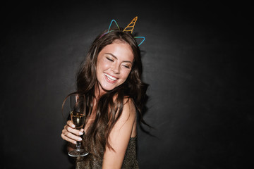 Image of young smiling woman holding glass of champagne while dancing