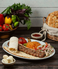 adana kebab on pita bread served with bulgur and onion slices