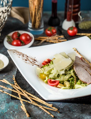 beef caesar salad plate garnished with parmesan and breadsticks