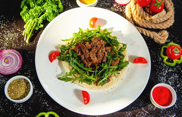 beef salad garnished with sesame on fresh arugula and flatbread
