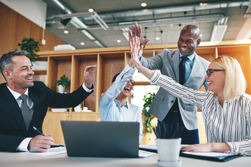 Diverse businesspeople laughing and high fiving together in an o