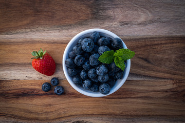 blueberries in a bowl on wooden table with a strawberry