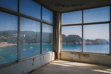 Large window of an abandoned hotel with the view to an ocean bay